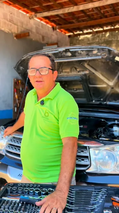 Profissional da oficina de camisa verde sorrindo ao lado do motor de um carro
